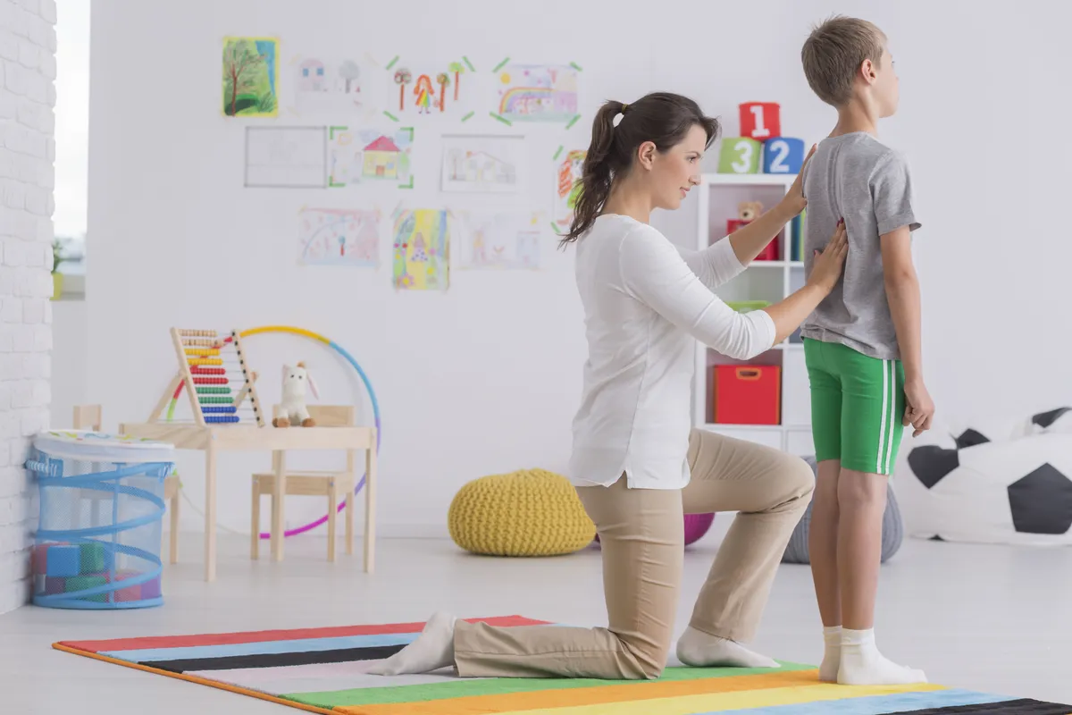 Young phsyiotherapist correcting body posture of a school-boy